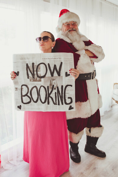 Appletini Photography standing with Santa holding a Now Booking sign.