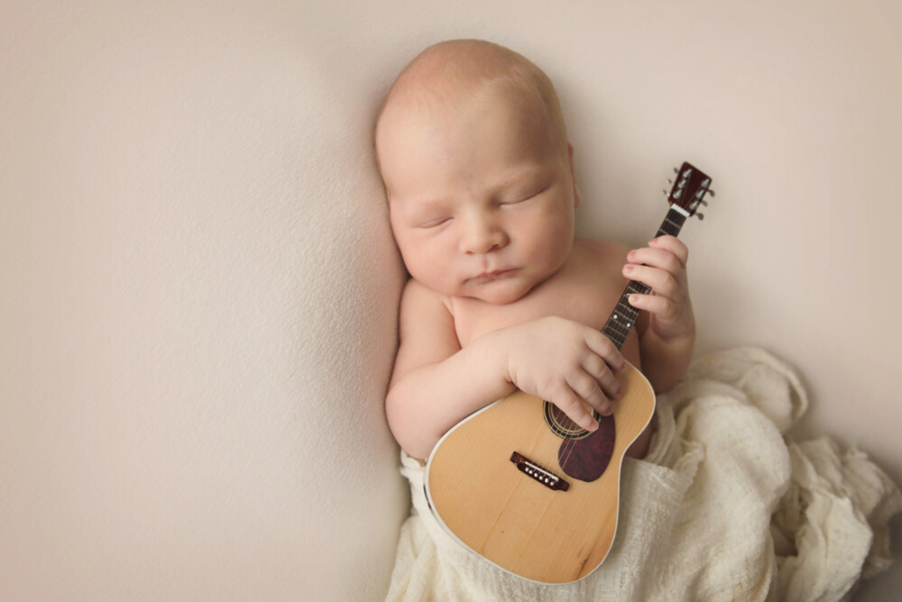Newborn holding a tiny guitar