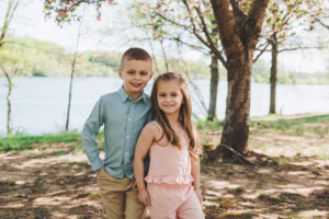 Two siblings laughing and running through tall grass at Core Creek Park during a spring family session