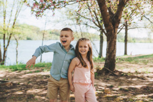 Two siblings laughing and running through tall grass at Core Creek Park during a spring family session