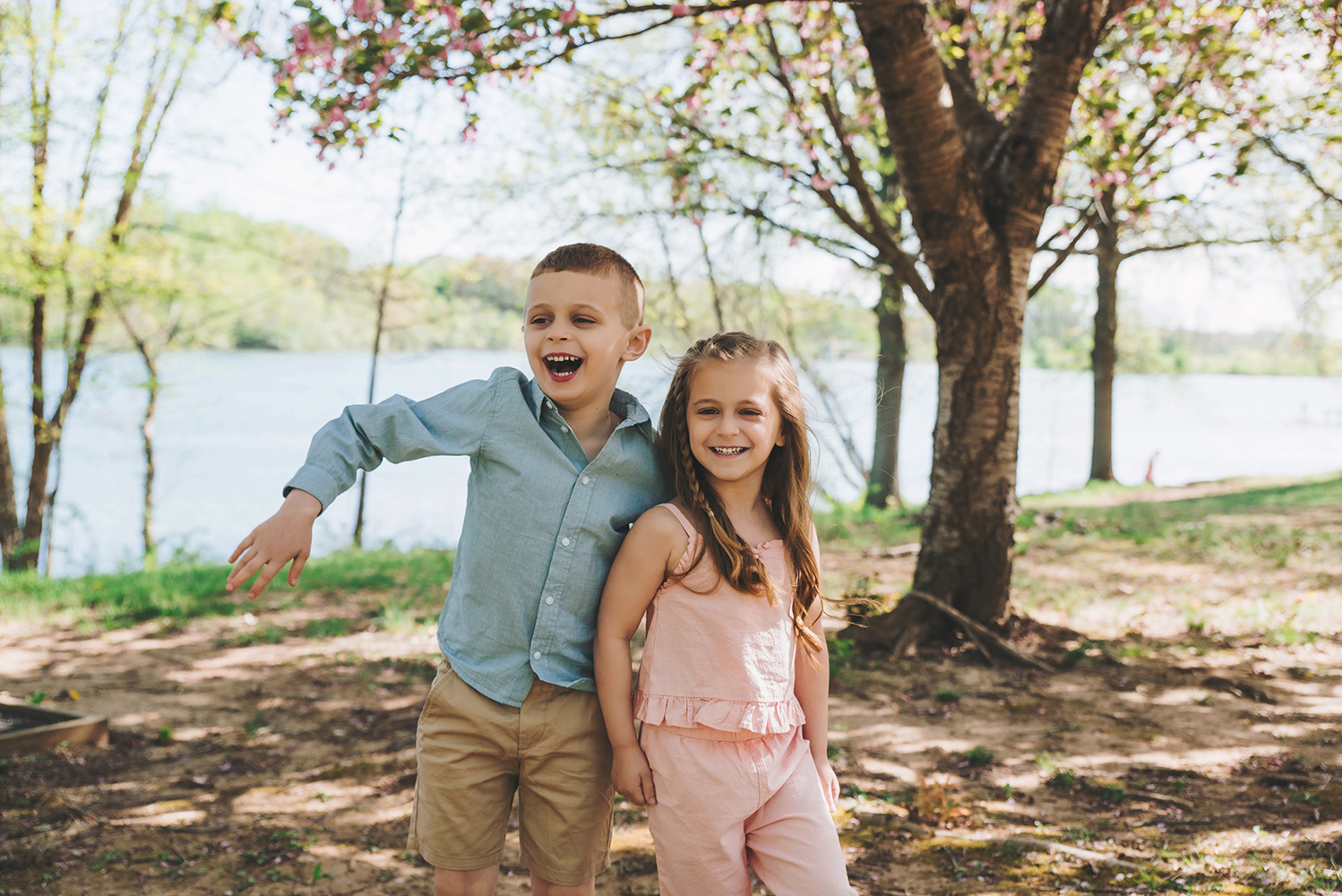 Two siblings laughing and running through tall grass at Core Creek Park during a spring family session